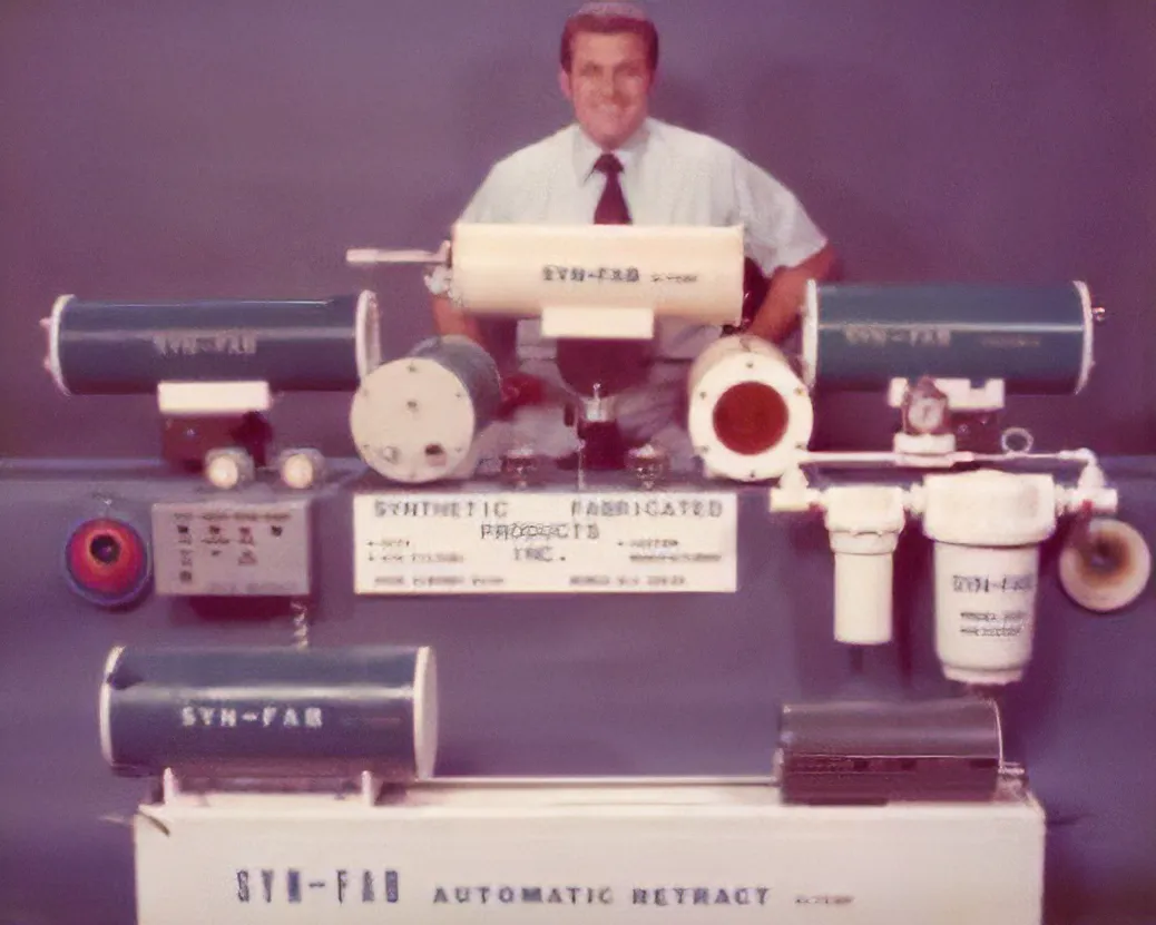Man in a shirt and tie standing behind a vintage laboratory machine with blue cylindrical components.
