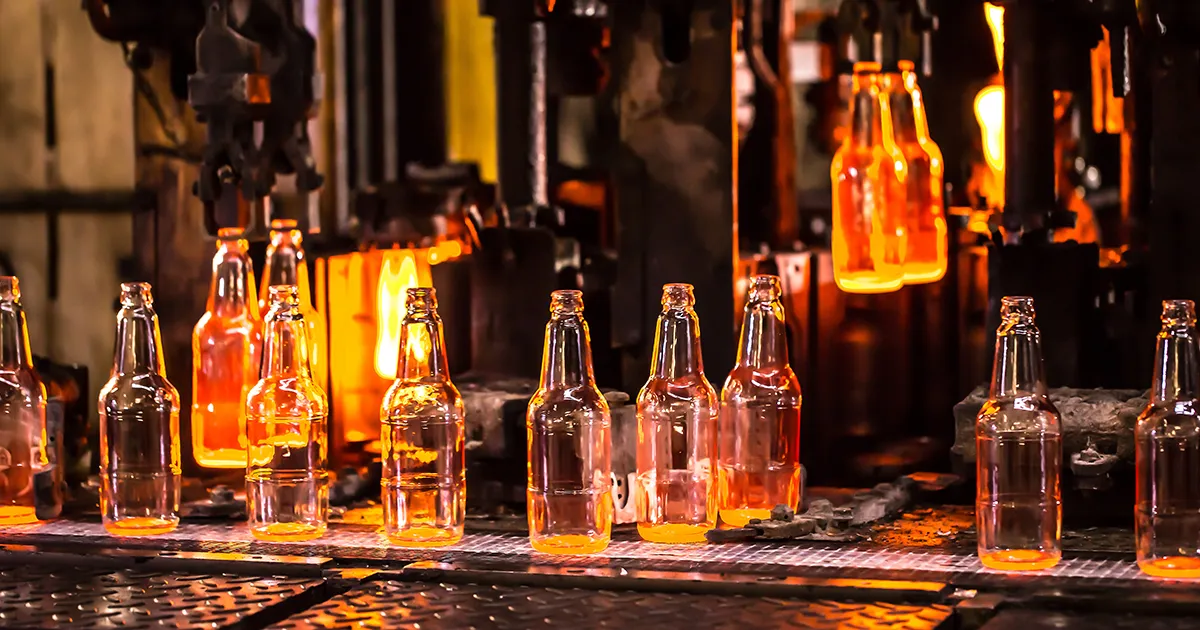 Glass bottles moving along a production line in a manufacturing facility, an environment monitored by Syn-Fab Inc. glass furnace camera systems
