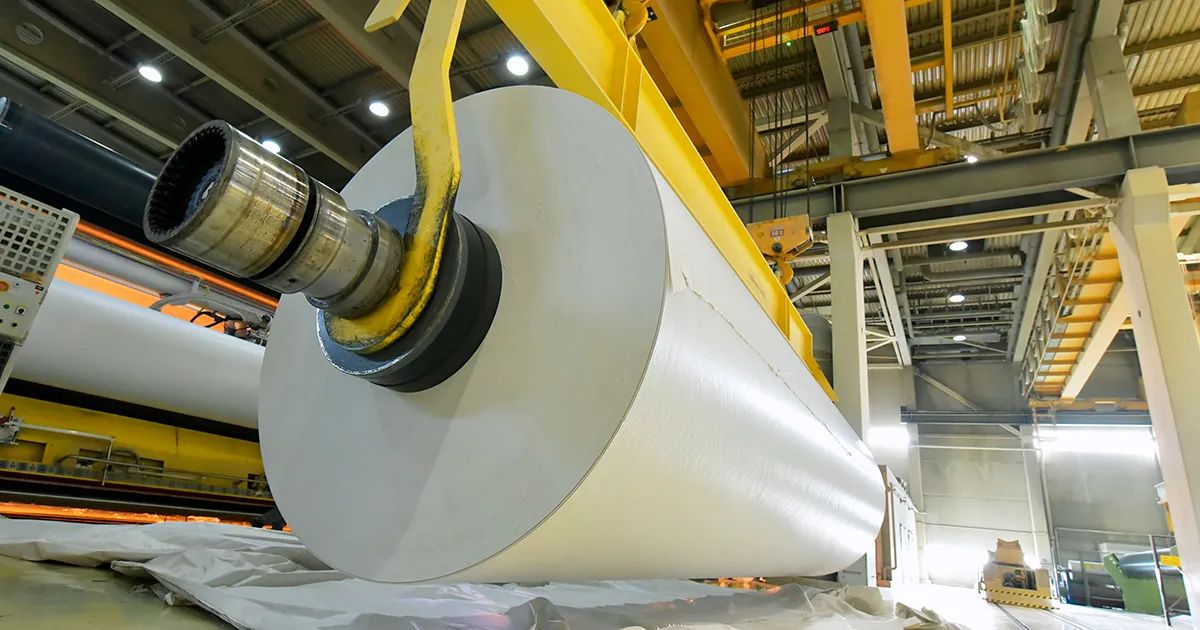A large paper roll on a spindle inside a manufacturing facility, an environment monitored by Syn-Fab Inc. paper mill camera systems