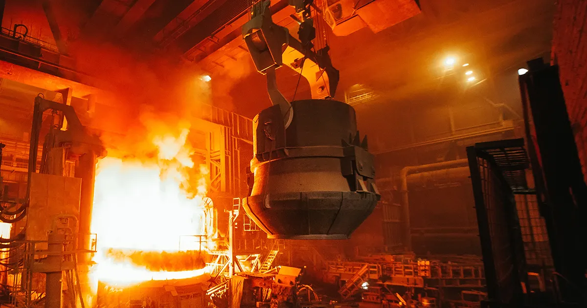 A large cauldron on a track moving through steam and smoke inside a manufacturing facility, an extreme environment monitored by Syn-Fab Inc. steel mill camera systems
